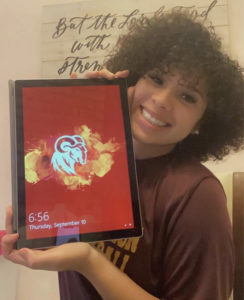 Smiling young Black woman in a maroon shirt holding up a tablet.